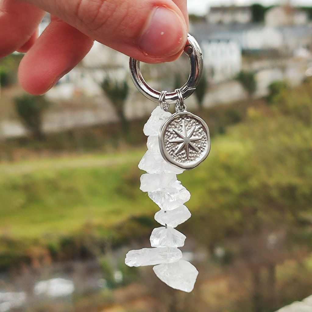 Hand holding a silver keychain featuring a cascade of raw rough-cut natural White Quartz chips and a textured silver star medallion.